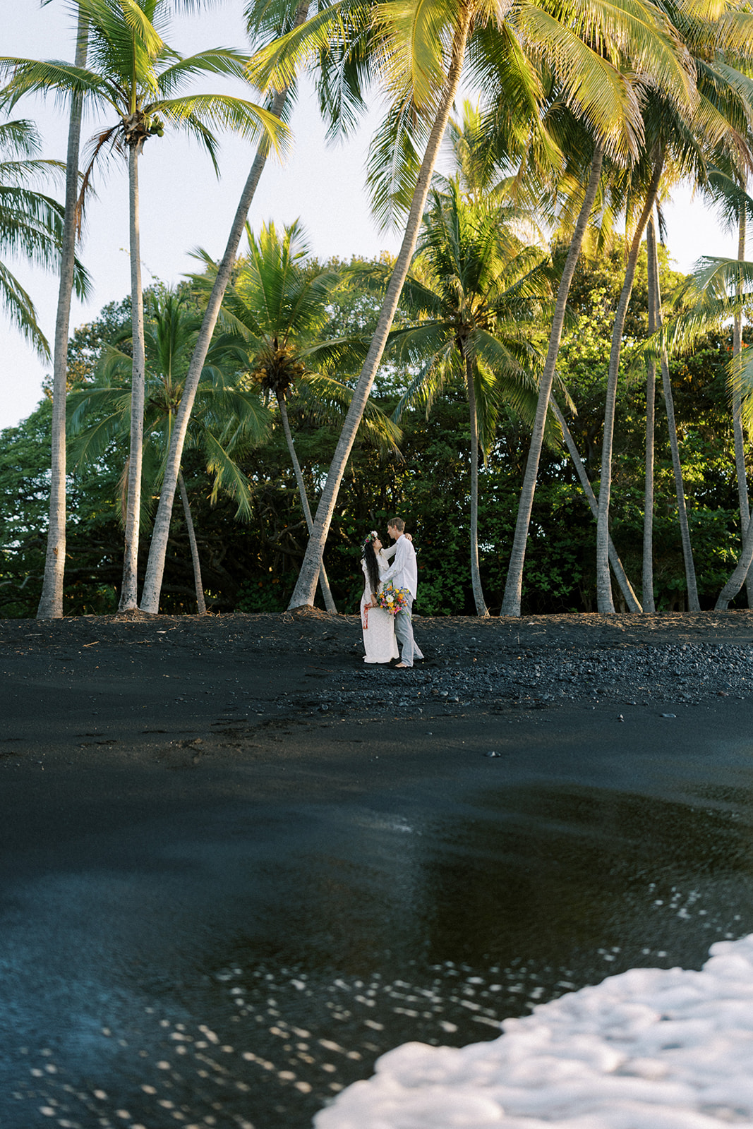 Couple standing during wedding at Punalu'u black sand beach.
